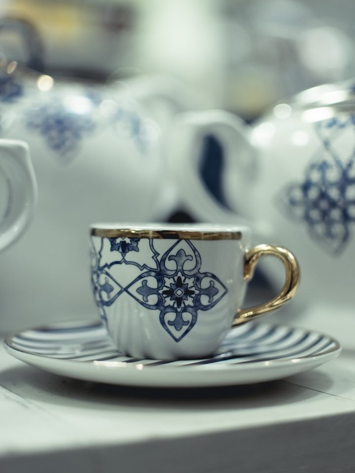 Zeitgeschenk Tasse mit goldfarbenem Henkel und blau-weißem Muster, auf einer Untertasse platziert.
